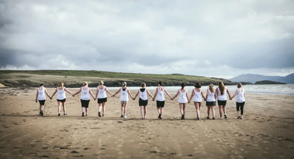 A group of women walking hand in hand on the beach.